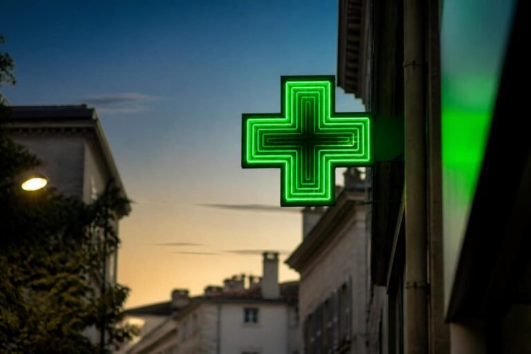 La croix verte d'une pharmacie allumée le soir dans une rue d'Alès