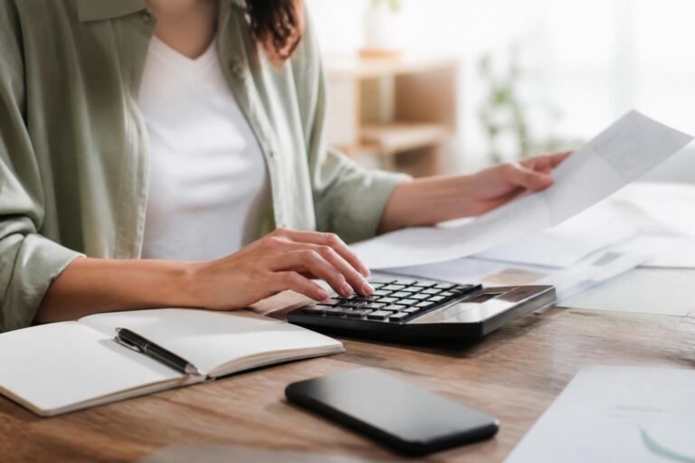 Personne calculant son budget familial avec une calculatrice et des documents sur une table