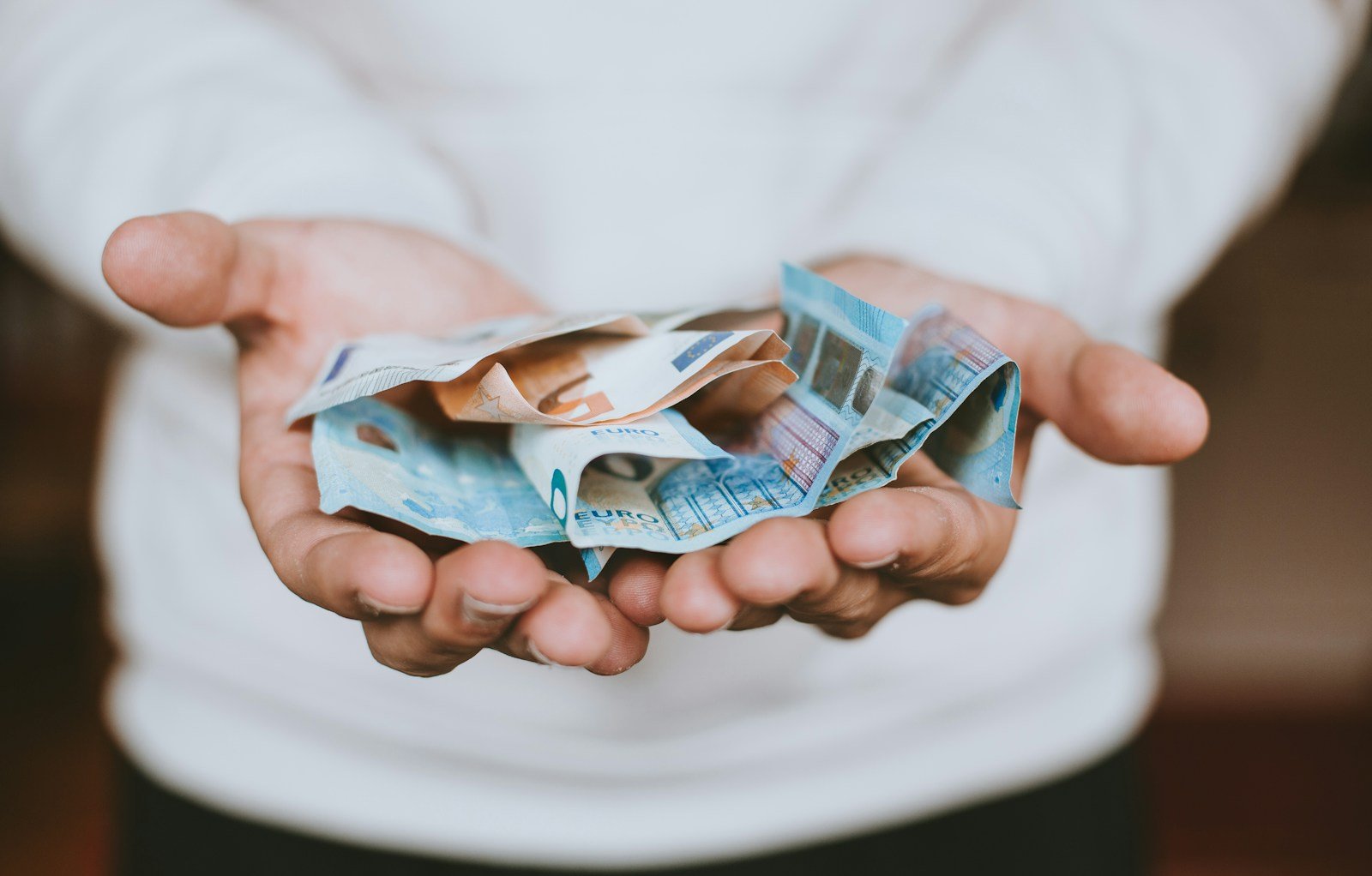 Personne examinant des billets en euros et des documents bancaires sur un bureau à la maison