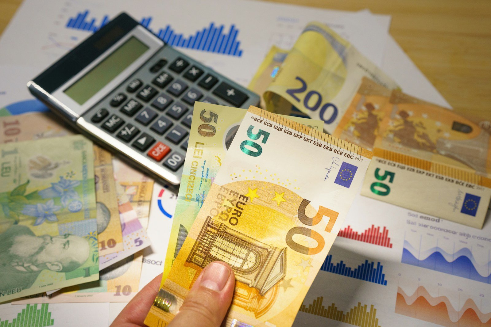 Personne examinant des relevés bancaires avec une calculatrice et des billets en euros sur un bureau